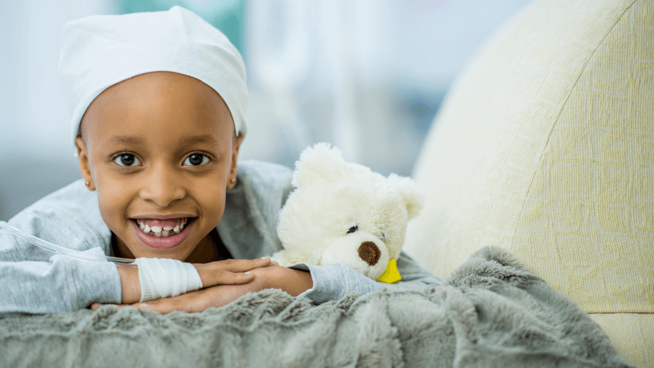 Child attached to an IV holding a teddy bear and smiling